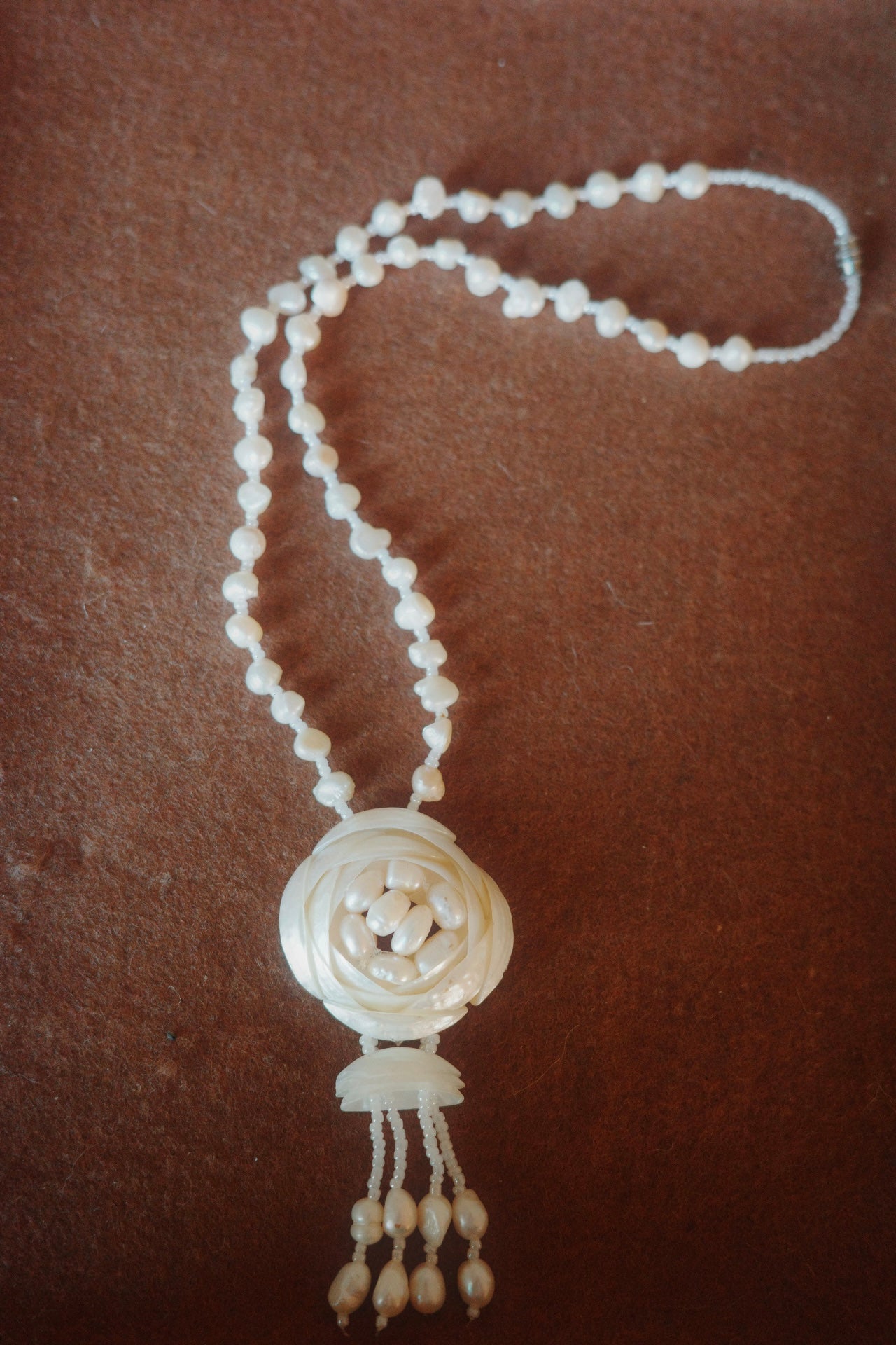 White beaded necklace with a decorative pendant on a brown background