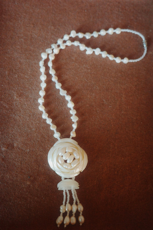 White beaded necklace with a decorative pendant on a brown background